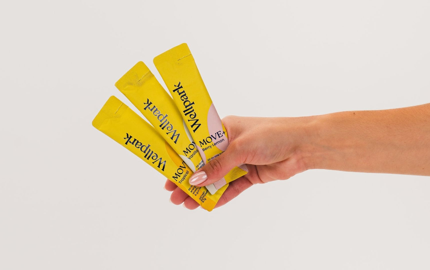 Hand holding three yellow sachets of Wellpark on a light gray background